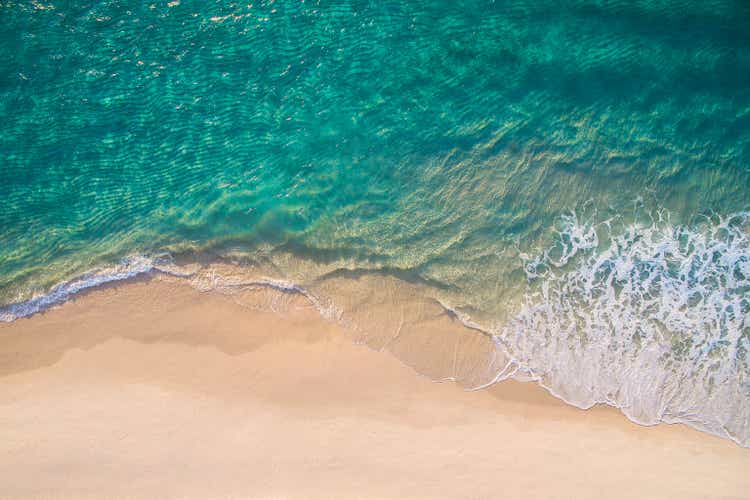 Clean ocean waves breaking on white sand beach with turquoise emerald coloured water