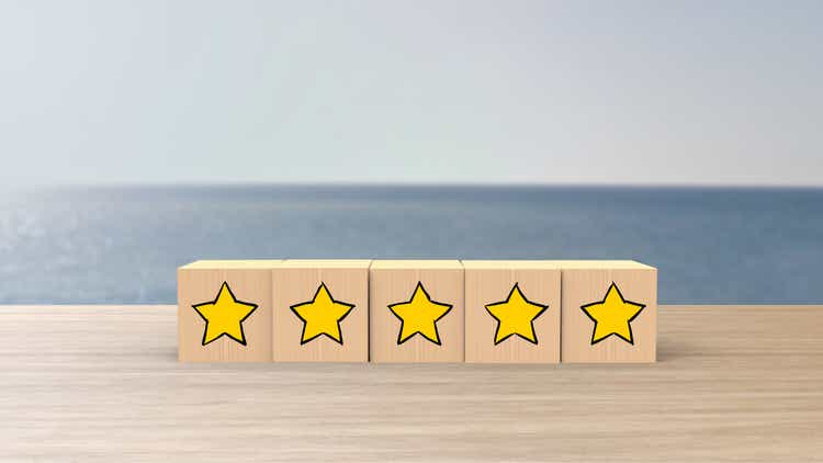 Wooden cartoon cube five yellow star review on blur sea with the sky background. Service rating, satisfaction concept. reviews and comments google maps, tripadvisor, facebook. online evaluations.