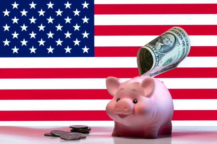 A piggy bank with a one USD bill against the background of the American state flag