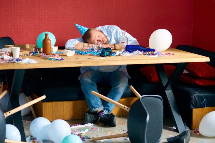 Man sleeping at table with blue cap in messy room after birthday party