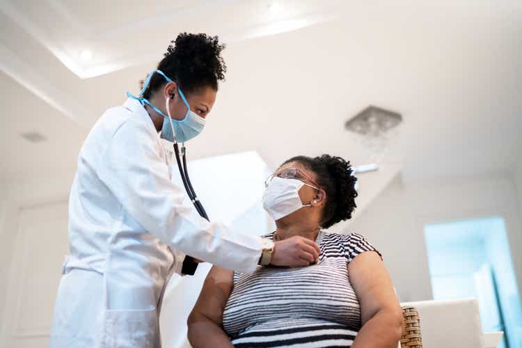 Doctor listening to patient"s heartbeat during home visit - wearing face mask