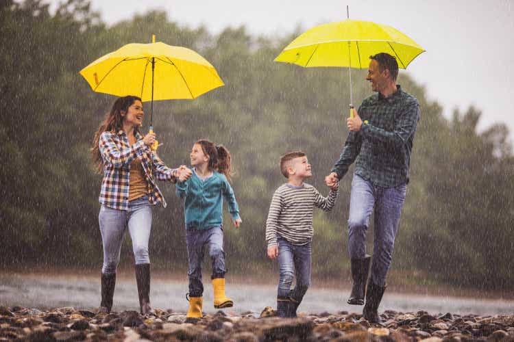 Happy family having fun while running on a rainy day at riverbank.