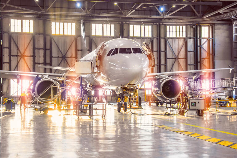 Uçak hangarındaki tüm uçak sistemlerinin işçi mekaniği ve diğer uzmanlar tarafından büyük ölçekli kontrolü. Garaj kapısının dışında parlak ışık.