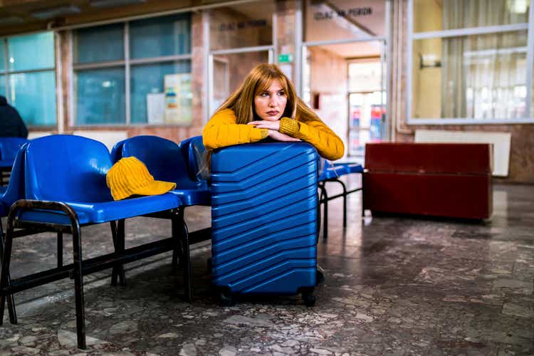 Young woman with suitcase sitting bored at train station