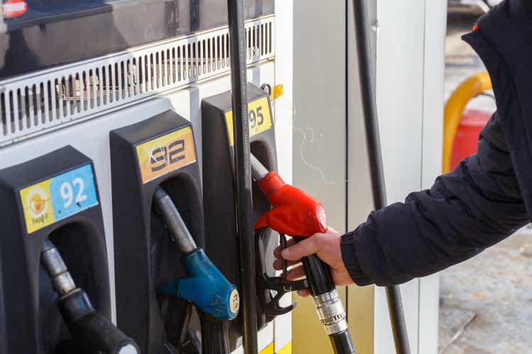 Old man hand taking red 95 gasoline fuel nozzle from gas station at day light.