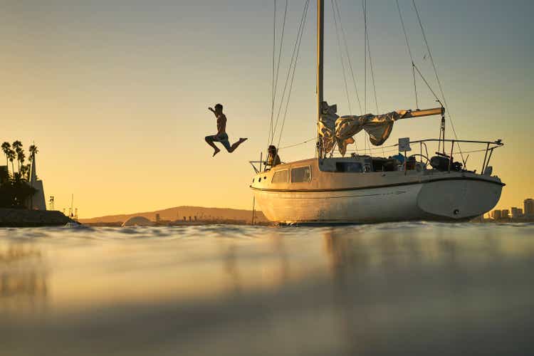 Man jumping into ocean from deck of sailboat at sunset