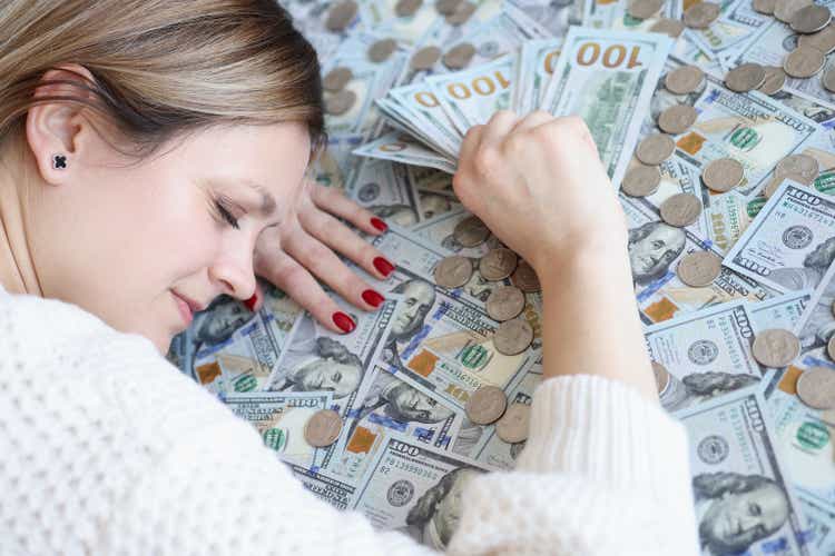 Woman with money in her hands sleeping on dollar bills