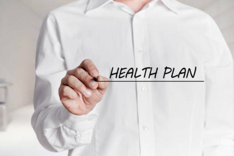 Man with pen writes the words health plan on a virtual screen.