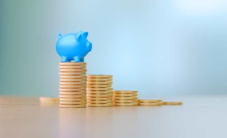 Savings Concept - Blue Piggy Bank Sitting On Coin Stacks Before Defocused Background