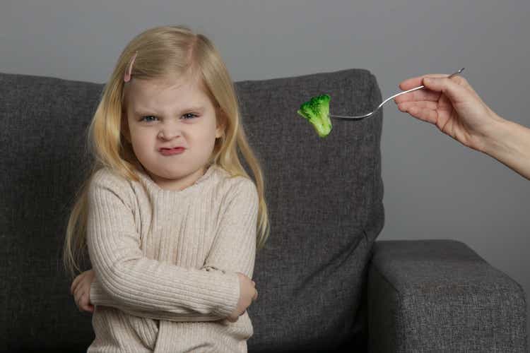 Little girl does not want to eat broccoli. Child refusing to eat vegetables.