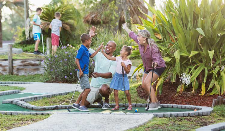 Interracial family, two children playing miniature golf