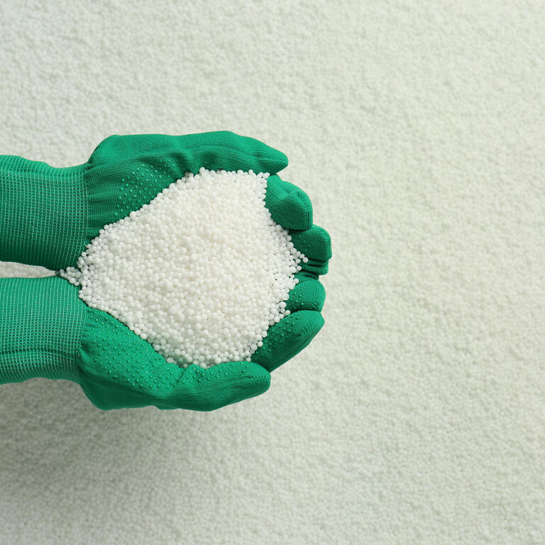 Woman holding pile of granular mineral fertilizer over grains, top view. Space for text