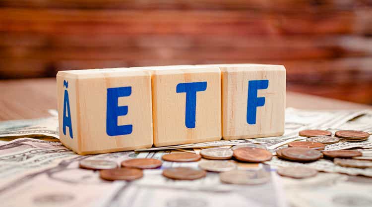 Wooden cubes with blue letters forming the word ETF (Exchange Traded Funds) on dollar bills on a table. Investment concept photo.