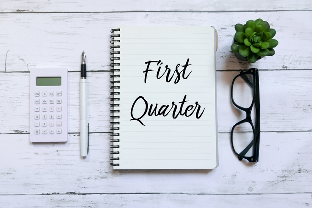 Top view of calculator,glasses,pen,plant and notebook written with First Quarter on wooden background.Business and finance concept.