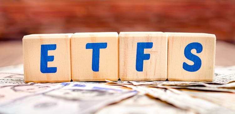 Wooden cubes with blue letters forming the word ETFS (Exchange Traded Funds) on dollar bills on a table. Investment concept photo.