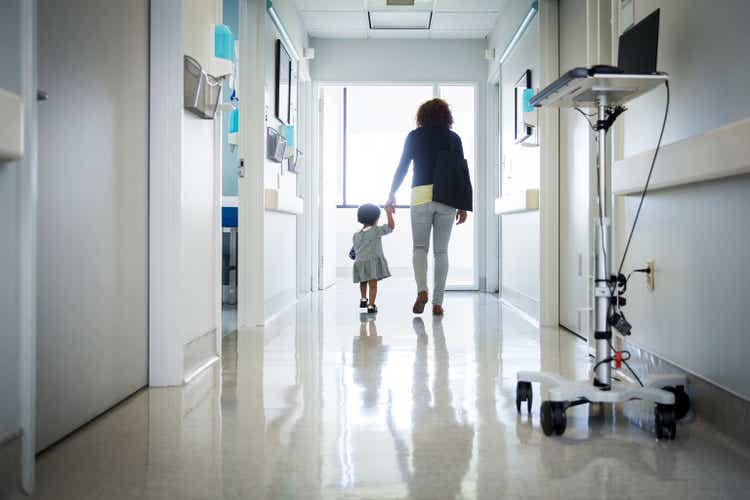 Rear view of mother and toddler walking in hospital corridor
