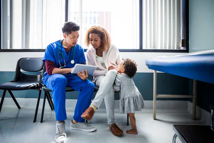 Male nurse showing digital tablet to mother by toddler in hospital