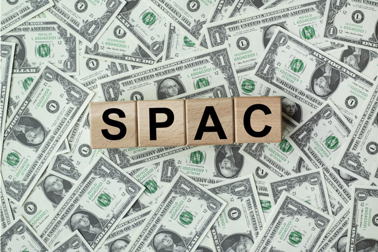 SPAC, special purpose acquisition company symbol. Wooden cubes with word "SPAC" on beautiful background from dollar bills, copy space. Business and SPAC, special purpose acquisition company concept.