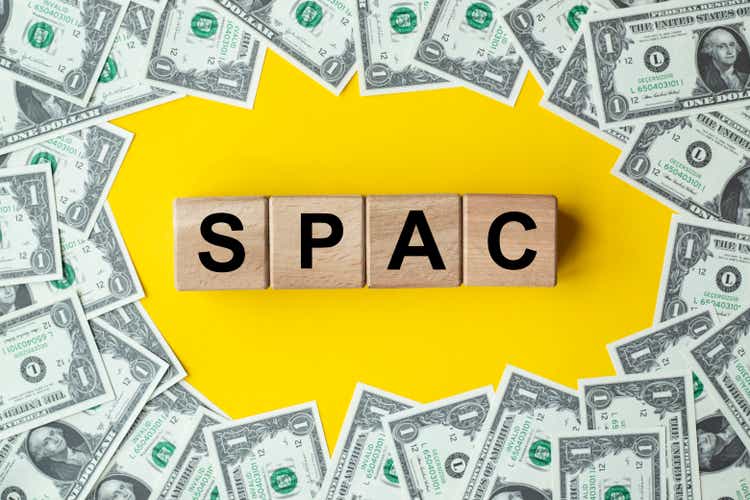 SPAC, special purpose acquisition company symbol. Wooden cubes with word "SPAC" on beautiful background from dollar bills, copy space. Business and SPAC, special purpose acquisition company concept.