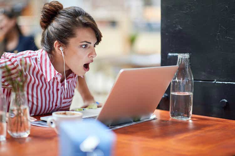 amazed young female watching content on her laptop with headphones in ears, can"t believe what she saw, with her mouth open. amazed, astonished reaction concept