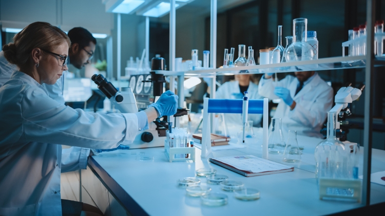 Team of Medical Research Scientists Work on a New Generation Disease Cure. They use Microscope, Test Tubes, Micropipette and Writing Down Analysis Results. Laboratory Looks Busy, Bright and Modern.