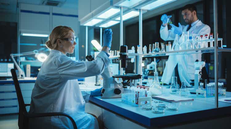 Female Medical Research Scientist Looks at Biological Samples Before Analysing it Under Digital Microscope in Applied Science Laboratory. Laboringenieur im weißen Mantel, der an Impfstoff en medicine and Medicine arbeitet.