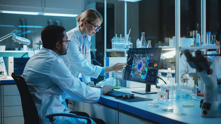 Female Research Scientist with Bioengineer Working on a Personal Computer with Screen Showing Virus Analysis Software User Interface. Scientists Developing Vaccine, Drugs and Antibiotics in Laboratory