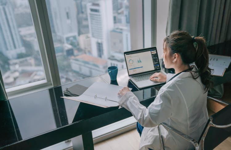 asian chinese female doctor working on medical report with laptop and document file