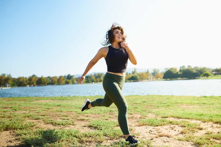 Smiling young woman jogging near lake on sunny day