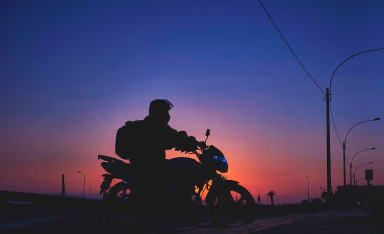 Night pizza delivery, man riding a motorcycle on the road at sunset