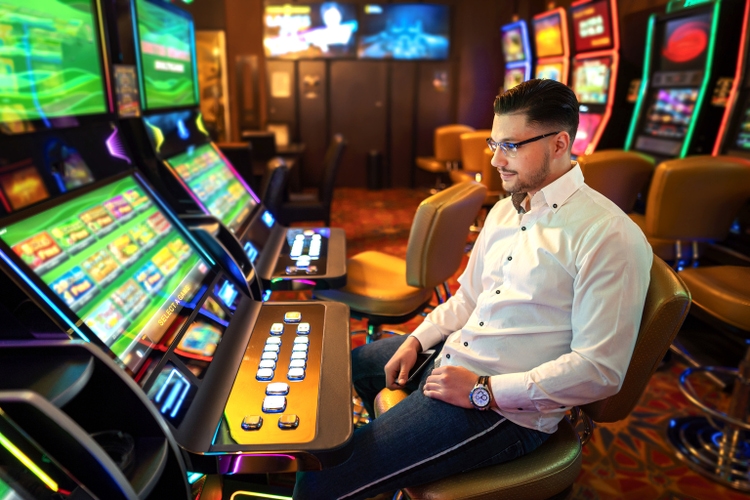 Young man sitting in a casino and gambling on a slot machine.