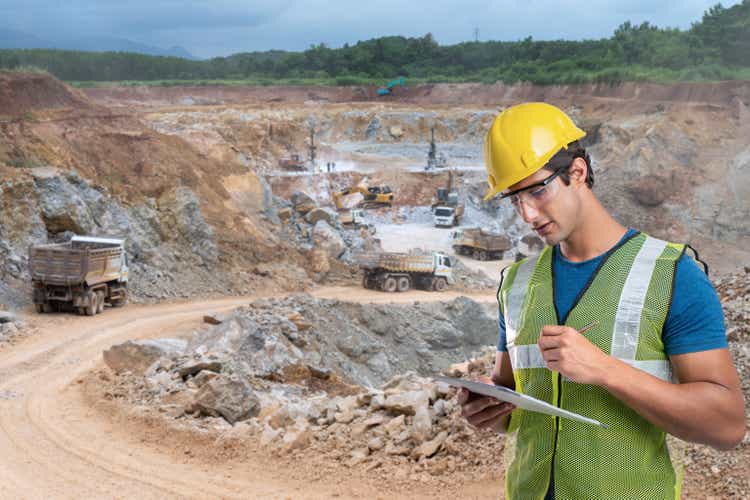 Side view shot of industrial workers wearing reflective jackets and hardhats standing on mining worksite outdoors using digital tablet, copy space