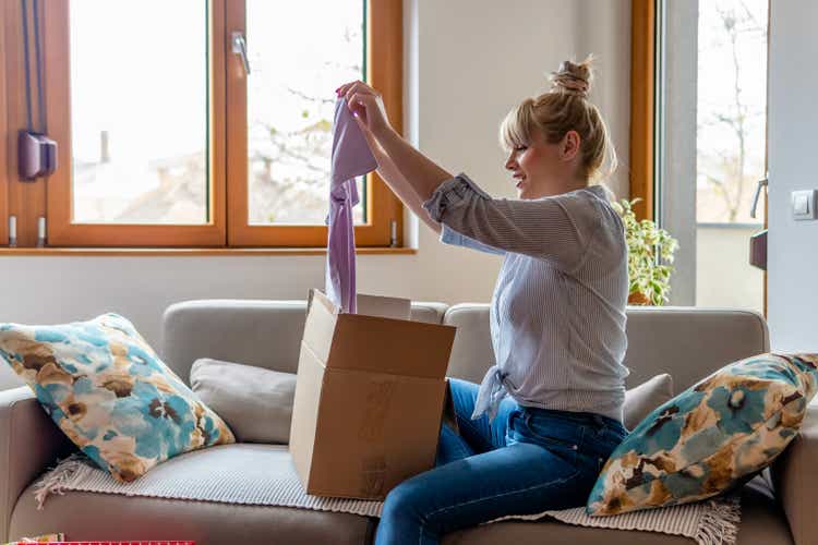 Happy young attractive woman open cardboard box satisfied with purchase online shop order sit on sofa at home.