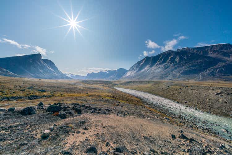 Stream winds through wild arctic landscape in Akshayuk Pass, Baffin Island, Canada. Moss valley floor and dramatic cliffs. Arctic summer in remote wilderness.