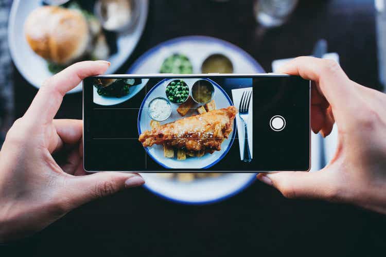 Woman photographing fish and chips in a restaurant with a smartphone