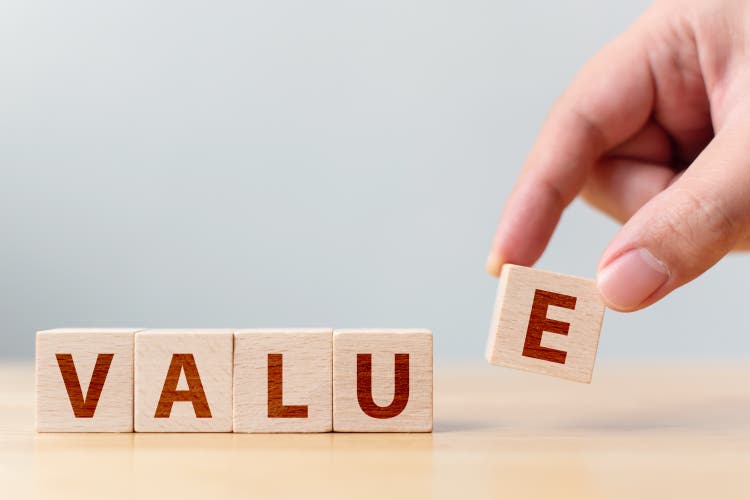 Hand of male putting wood cube block with word “VALUE” on wooden table