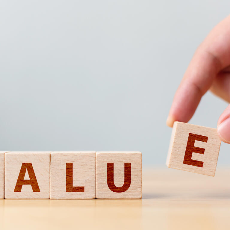 Hand of male putting wood cube block with word “VALUE” on wooden table