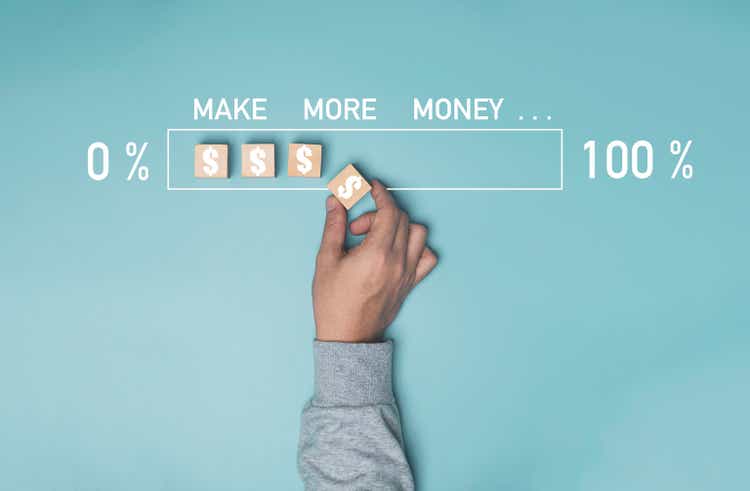 Businessman hand putting dollar sign which print screen on wooden cube block on blue background for increase percentage of loading make more money concept.