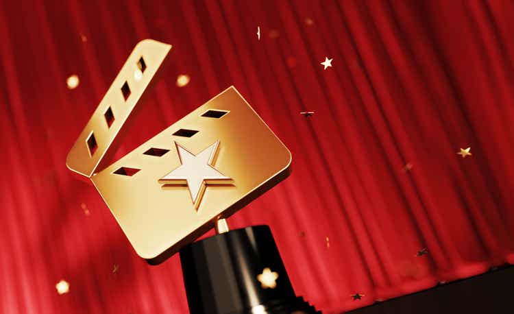 Gold Colored Confetti Falling Onto A Gold Award With Star Shape Sitting Before Red Stage Curtain