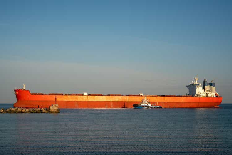 Großes Hochseefrachtschiff in Orange. Das trockene Frachtschiff gelangt mit einem Schlepper in den Hafen.