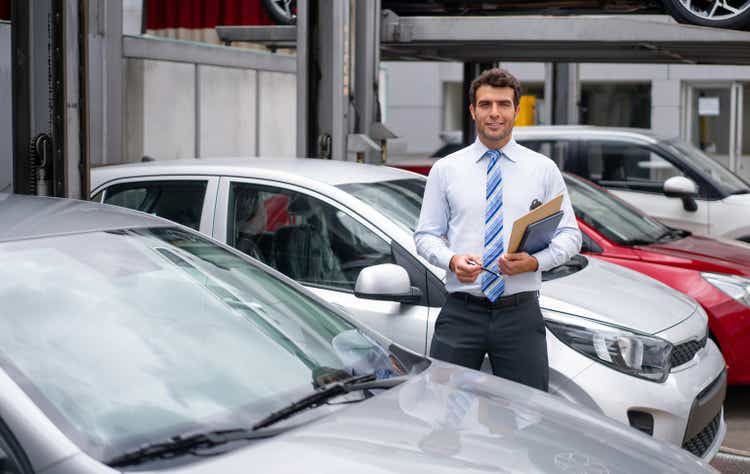 Portrait of a salesman working at the dealership showing cars outdoors