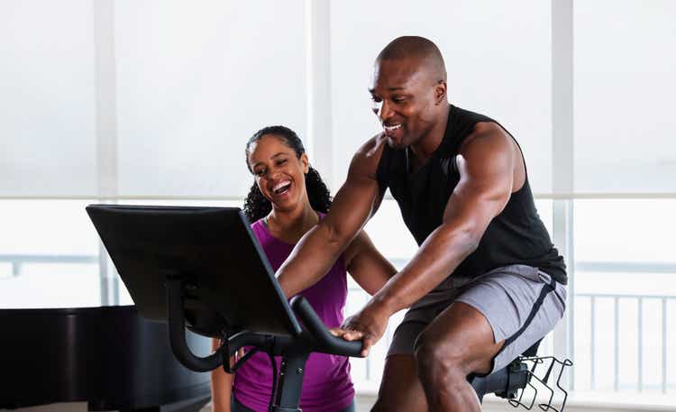 Man on exercise bike at home, supportive partner