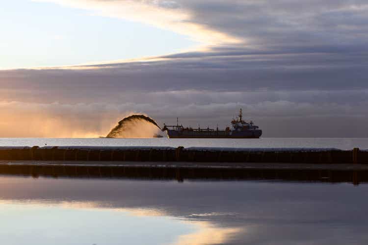 Vessel engaged in dredging at sunset time. Hopper dredger working at sea. Ship excavating material from a water environment. Beautiful sunset.