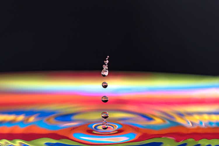 Water drop making ripple on multicolored base and black background