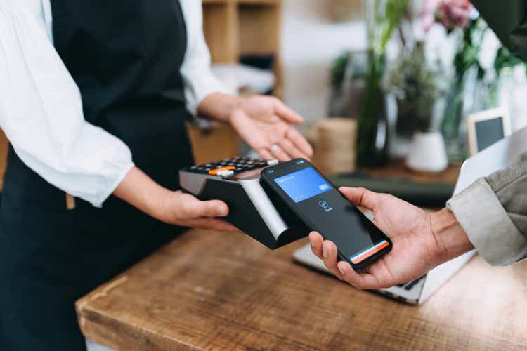 Close up of young Asian man shopping at the flower shop. He is paying with his smartphone, scan and pay a bill on a card machine making a quick and easy contactless payment. NFC technology, tap and go concept