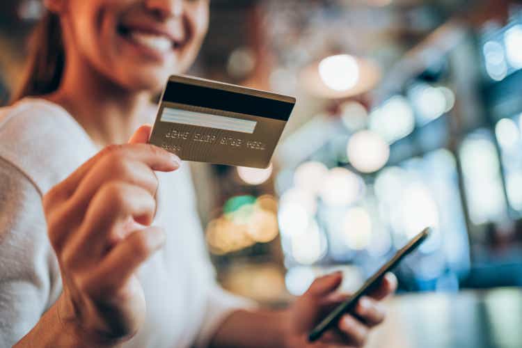 Woman using smart phone and credit card for online shopping in city cafe.