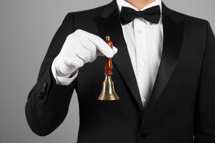 Butler holding hand bell on grey background, closeupu