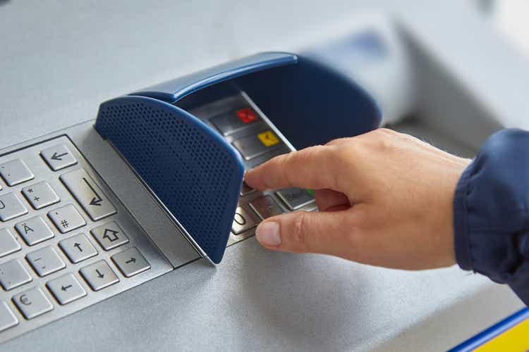 A female hand dials a personal code on the ATM keyboard openly. The concept of lack of caution, carelessness, money transfers and theft of personal information. Close-up