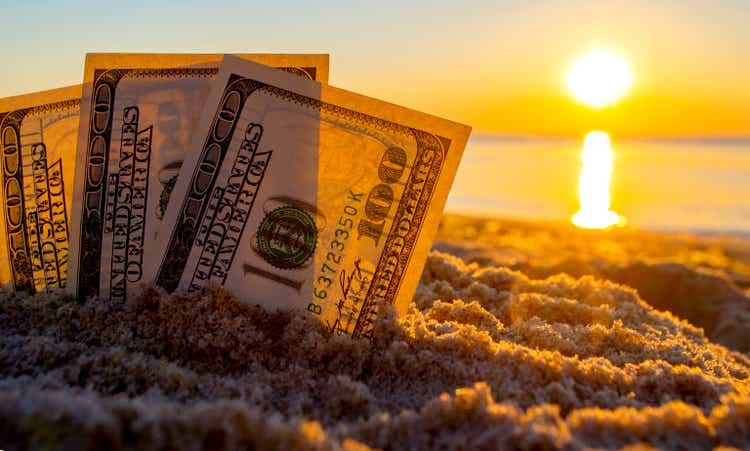 Three dollar bills are buried in sand on sandy beach near sea at sunset dawn