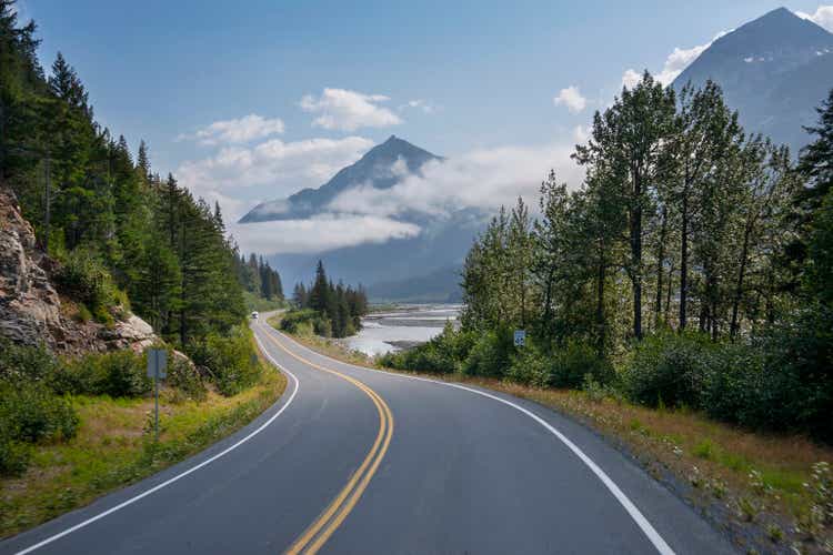 Camper travels along a curving highway in Alaska below mountains near Seward on a sunny afternoon